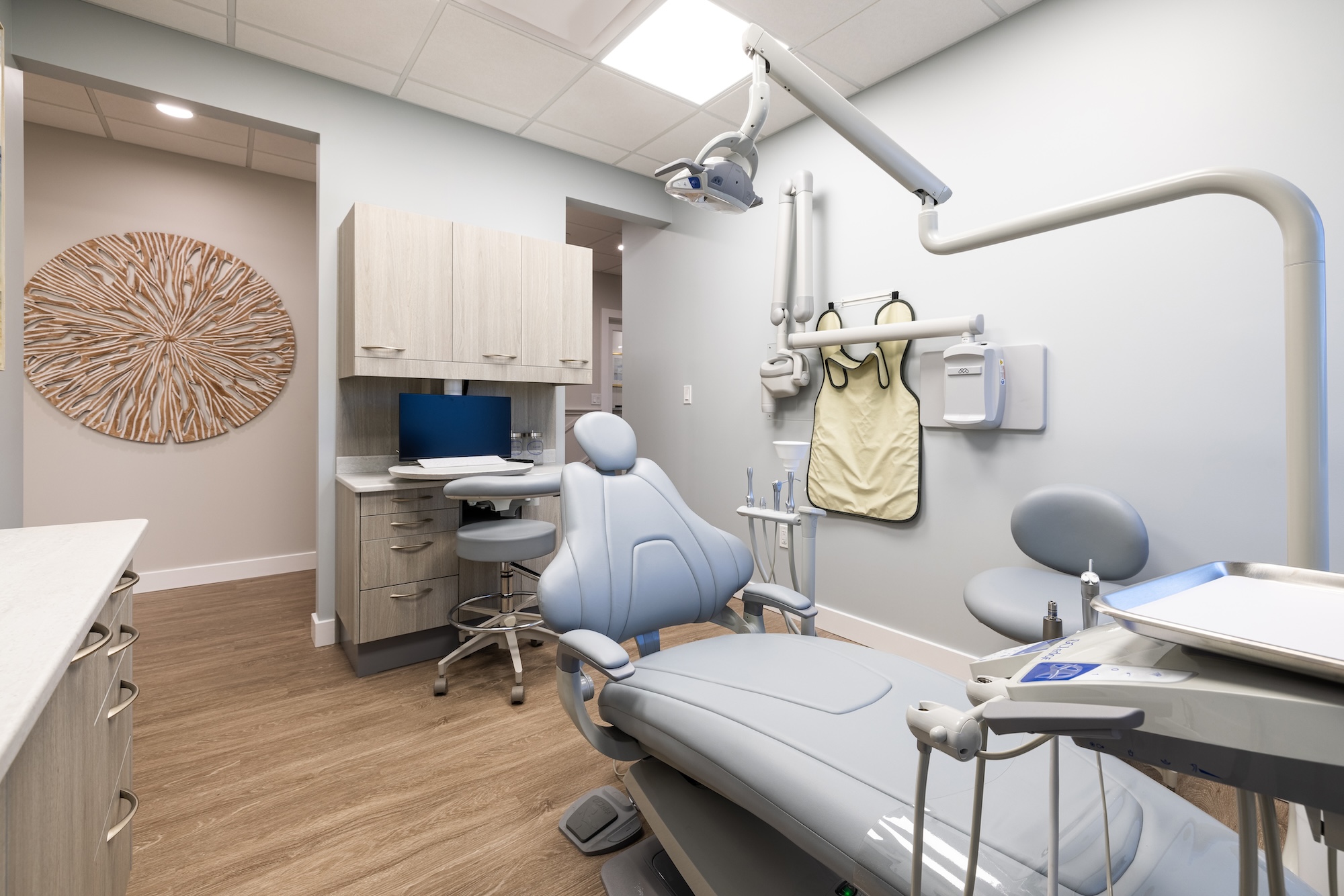 The image shows an interior view of a dental office, featuring a chair, desk, and equipment commonly found in such a setting.