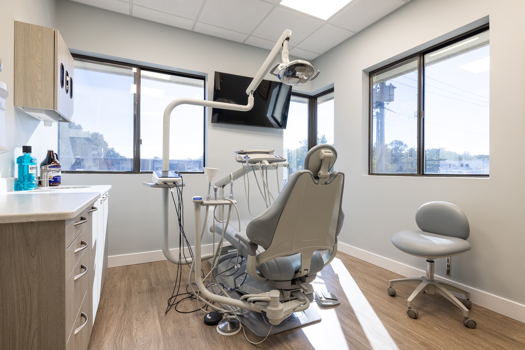 The image shows a dental office interior with a dental chair, equipment, and a window view.