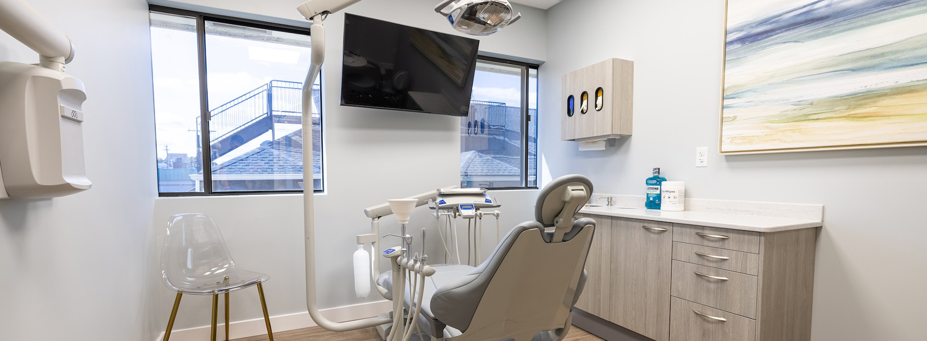 A person is seated in a dental chair, receiving care from a dental professional who stands behind them.