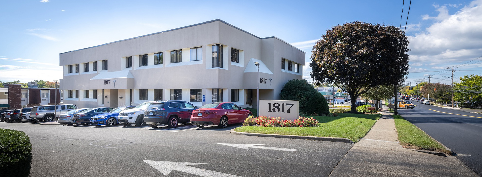 A large, modern two-story building with a parking lot in front, featuring multiple cars parked.