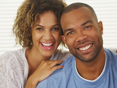 The image shows a man and woman posing for a photo with smiles, the man is wearing a short beard and has his arm around the woman.